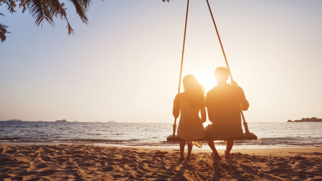 Coppia seduda su un'amaca in spiaggia che rappresenta l'articolo: la fiamma gemella ti ama?